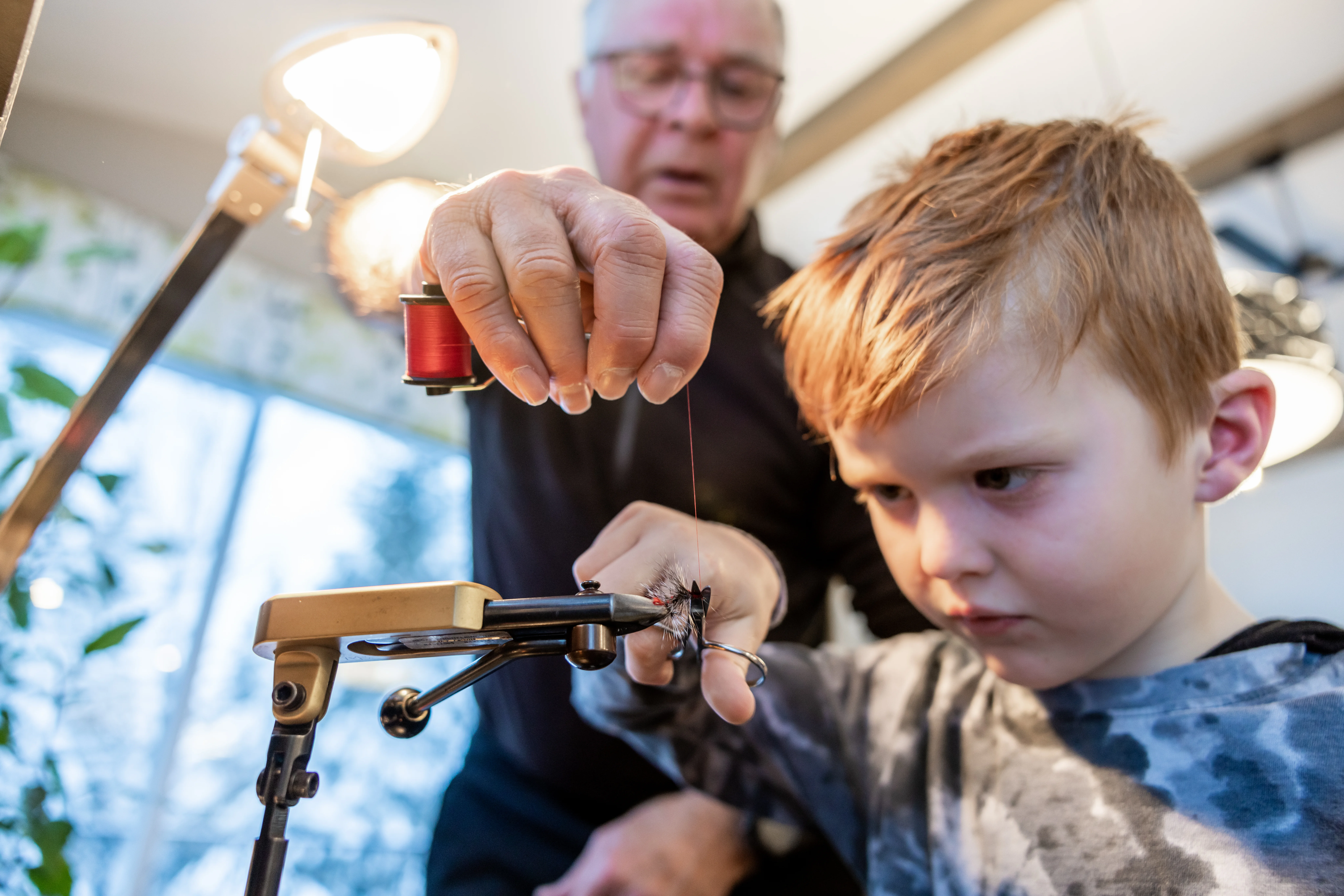 Grandfather teaching grandson to tie a fly
